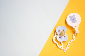 baby blue pacifier with a pin on a colored yellow and blue background, copy space