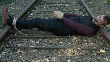 Tied Up Businessman Trying to Free Himself on a Rail Tracks