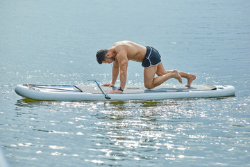 Side view of fit man doing fitness exercises sitting on sup board.