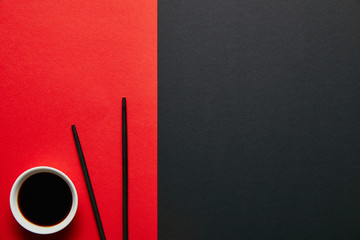 top view of soya sauce in bowl and chopsticks on red and black background