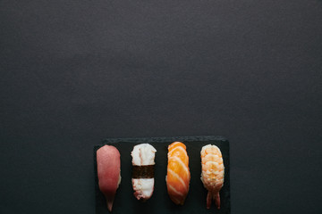 top view of assorted nigiri sushi set on black slate plate on dark tabletop