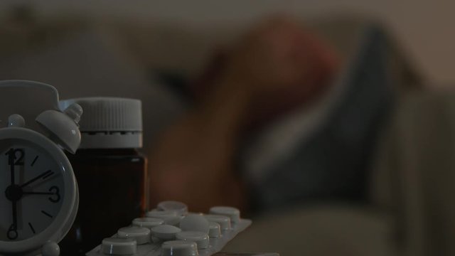 Medicine Pills and a Sick Man Resting in Bad in Blurred Image