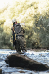 Fly fisherman using flyfishing rod in beautiful river