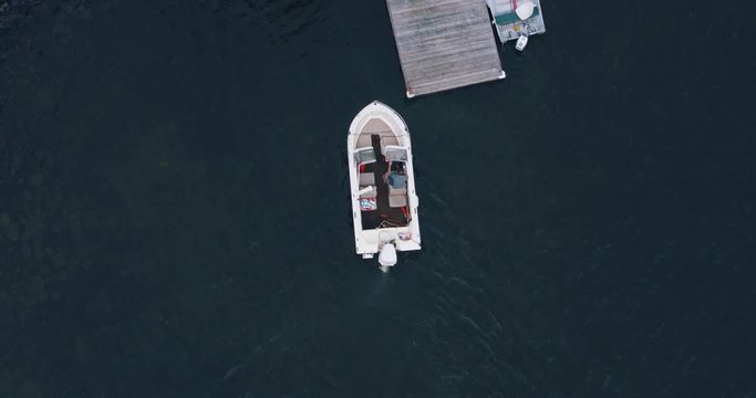 Overhead shot of young man docking outboard motor boat at wooden dock on lake