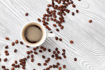 cup of coffee with coffee's beans over white wooden background, top view