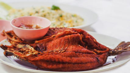 Closeup Shot of Tasty Deep Fried Fish in A White Ceramic Dish, Served with Spicy Sauce with Fried Rice in The Background (Selective Focus and Blurred Background).