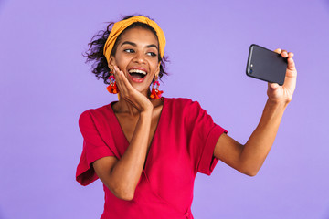 Joyful african woman in dress making selfie on smartphone