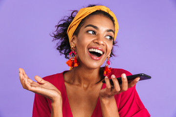 Cheerful african woman in dress talking by smartphone