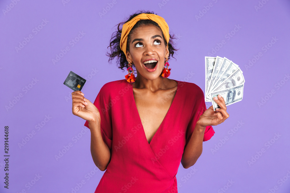 Wall mural cheerful african woman in dress holding money and credit card