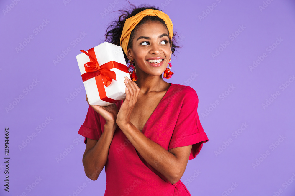 Poster Cheerful woman in dress holding gift box and looking away