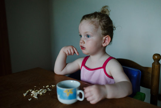 Little Girl Eating Nuts And Looking Confused At The Kitchen Table