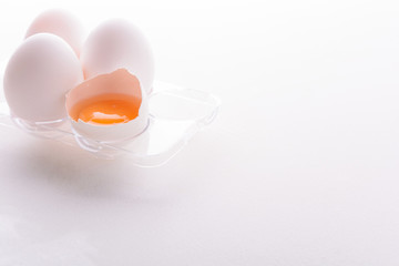 Broken egg with whole eggs in a transparent plastic container on white wooden background