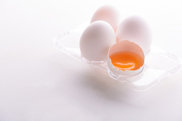 Broken egg with whole eggs in a transparent plastic container on white wooden background