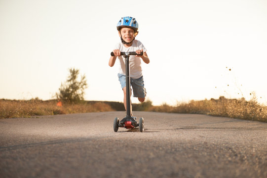 healthy little boy in helmet riding scooter on road with high speed outdoor