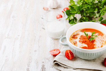Bowl of homemade tomato soup with cream and parsley on wooden table. Copy spase for your text