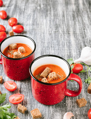 Red mug of homemade tomato cream soup with crackers or crouton and parsley on wooden table. Copy spase for your text