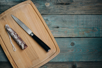 top view smoked sausage, salami, knife on cutting Board, wooden background