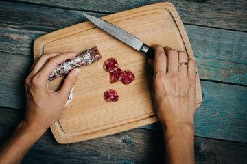 top view woman hands, salami, knife on cutting Board, wooden background