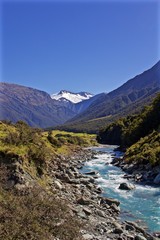 Naklejka na ściany i meble A Blue River Flows Down the Valley Through New Zealand from a Snow Capped Mountain