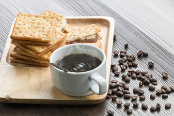 Black coffee,cracker and coffee bean on wood with warm morning light.Copy space.