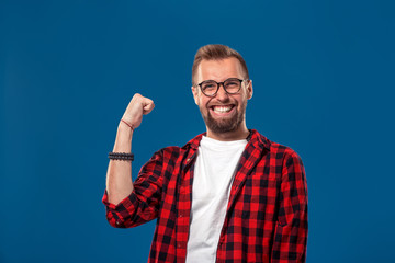 Trendy man in checkered shirt holding fists up in gesture of success and screaming happily with win...