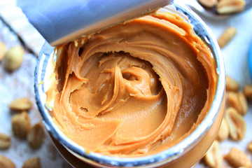 Peanut butter in a glass jar on a wooden table with peanuts.