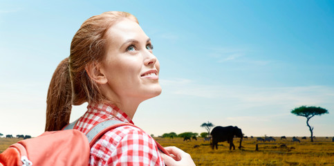 adventure, travel, tourism, hike and people concept - smiling young woman with backpack over animals in african savannah background
