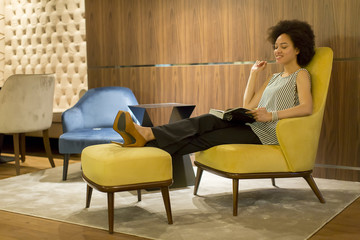 Young woman sittinh on a yellow chair and reading a book