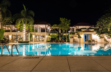 Tropical swimming pool with lighting and main building in hotel