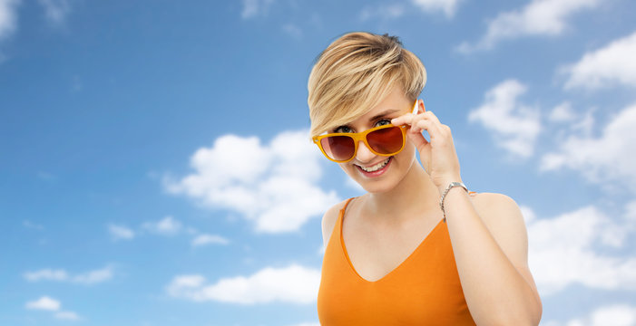 summer fashion, style and eyewear concept - portrait of happy smiling young woman in sunglasses over blue sky s background