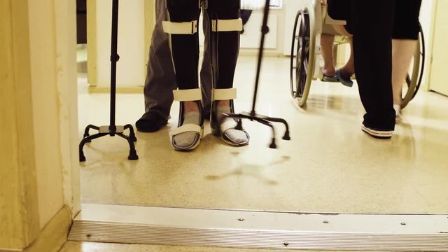 Close up legs of disable man in orthosis walking with support of two walking cane in the rehabilitation clinic. Doctor helping him.
