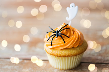 food, baking and holidays concept - cupcake or muffin with halloween party decorations on wooden...