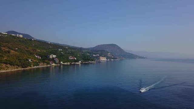 Aerial drone footage of speed boat cruising in blue water. Mountains and sea on background. European landscape. Camera moves forward. Crimea, Utes , Black Sea.