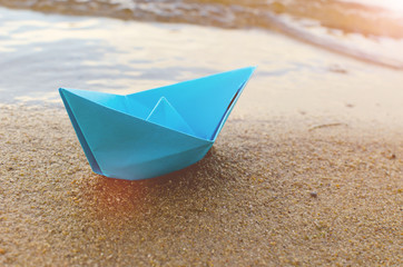 Blue paper boat in the sand on the ocean, early morning.