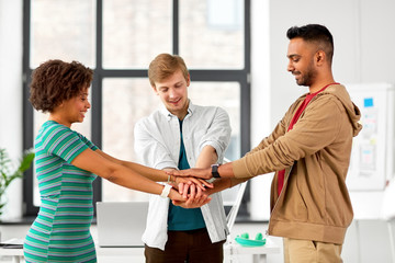 business, teamwork and corporate concept - happy creative team stacking hands together at office