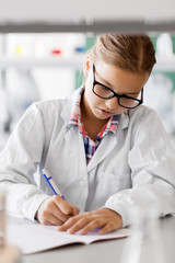 education, science and children concept - close up of girl studying chemistry at school laboratory and writing to workbook