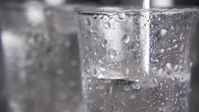 Slow motion in the foreground in a glass with drops of water to pour vodka and on a background blurred vodka in the misted glasses close-up.