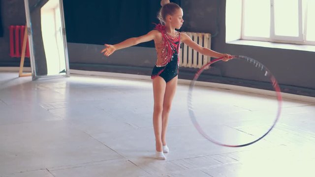 Gymnast girl performing elements with hula hoop at dance studio
