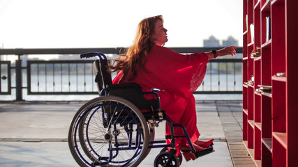 Beautiful Red-Haired Girl In A Wheelchair Takes Out Of The Shelf Book