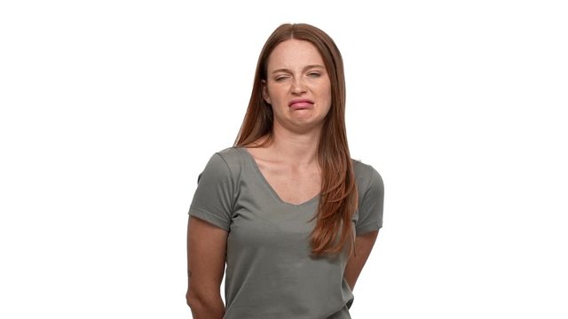 Portrait of discontent ginger woman twisting mouth and looking with disgust and aversion, isolated over white background slow motion. Concept of emotions