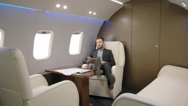 Portrait of lawyer succesful man taking a seat in his private plane and entrepreneur reading news on his tablet. Concept of: business people, plane flying, tablet reading.