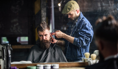 Barber with clipper trimming hair on nape of client. Hipster lifestyle concept. Hipster client getting haircut. Barber with hair clipper works on haircut of bearded guy barbershop background