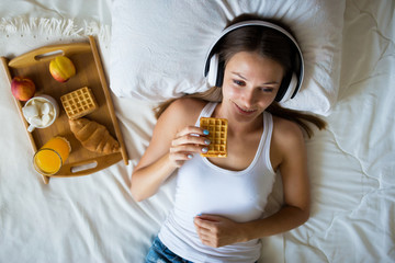 Beautiful brunette girl listening to music on headphones in bed . Breakfast Woman in the morning