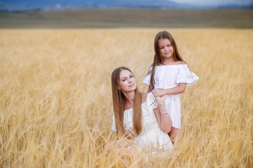 Beautiful family in a field of rye at sunset. A woman and child in amazing clothes walking through the field of rye.