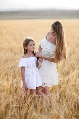 Beautiful family in a field of rye at sunset. A woman and child in amazing clothes walking through the field of rye.