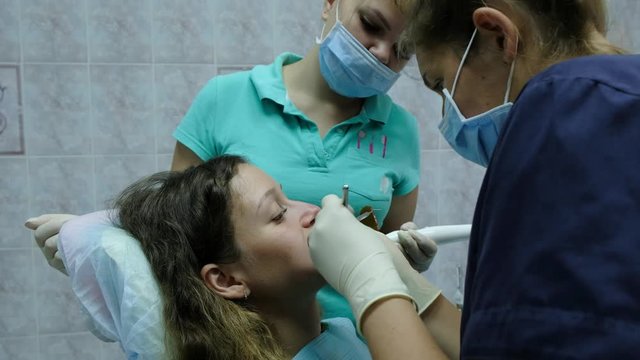 Visit to the dentist. Orthodontist doctor with assistent sets up iron braces for a woman with a dental fixator