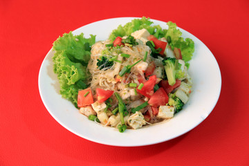 Cellophane noodles salad with Vietnamese Pork Sausage and variety vegetable such as lettuce, tomato and onion in the round plate on the red floor.