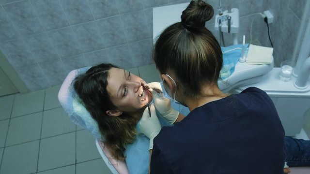 Visit to the dentist. Orthodontist doctor sets up iron braces for a woman with a dental fixator, top view