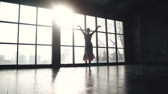 ballet dancer dancing a classical ballet in pointe shoes on the background of a large window. Elegant ballerina in pointe shoes and a long fluttering dress. slow motion