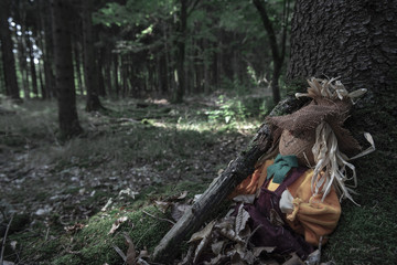 Scarecrow covered in dried leaves at a tree root
